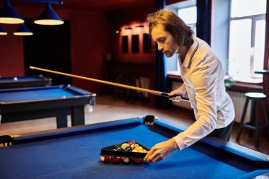 A man in a casual white shirt sets up a game of billiards in a dimly lit pool hall. clipart