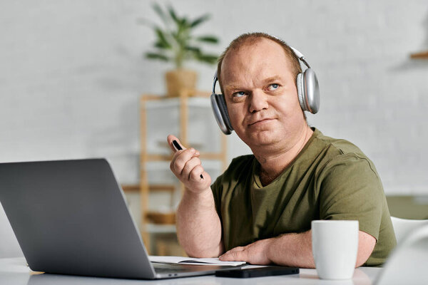 A man with inclusivity wearing headphones sits at his desk in his home office working.