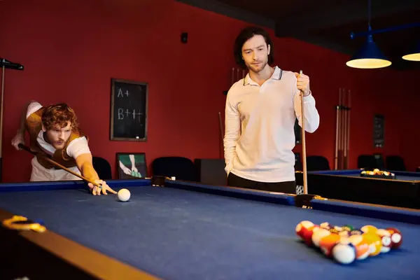stock image Friends play pool in a dimly lit room, one lining up a shot while the other waits his turn.