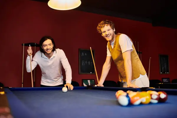 stock image Two men in casual clothing play pool together in a dimly lit room.