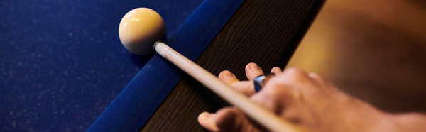 Крупный план руки, держащей бильярдный кий, готовый ударить белый бильярдный шар по синему столу для бильярда.