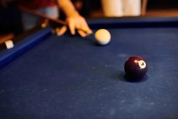 Stock image A close-up shot of a billiard ball on a blue felt table, with a blurred figure in the background.