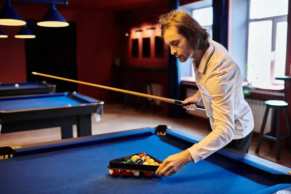 stock image A man in a casual white shirt sets up a game of billiards in a dimly lit pool hall.