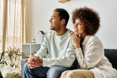 An attractive African American couple sits on a couch at home, using sign language to communicate. clipart