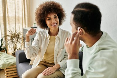 Gülümseyen bir Afro-Amerikan çifti evlerinde kanepede otururken işaret diliyle iletişim kuruyor..