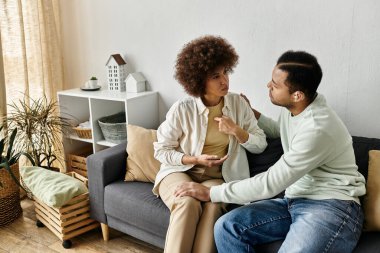 A couple sits on a couch at home, using sign language to communicate. clipart