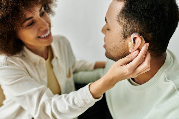 Кудрявая афроамериканка помогает мужу со слуховым аппаратом дома.