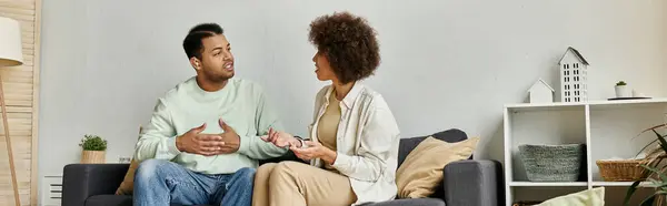 stock image An African American couple sits on a couch, using sign language to communicate at home.