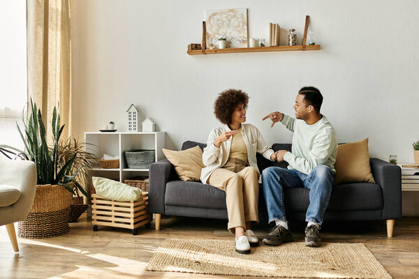 Афроамериканская пара сидит дома на диване и общается на языке жестов.