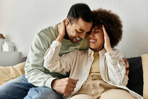 An African American couple sits on a couch, using sign language to communicate, and both smiling widely.