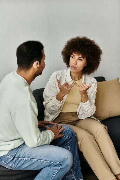 stock image A couple sits on a couch, the woman signing to the man.