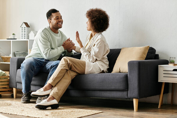Афро-американская пара сидит на диване в своем доме, используя язык жестов для общения.