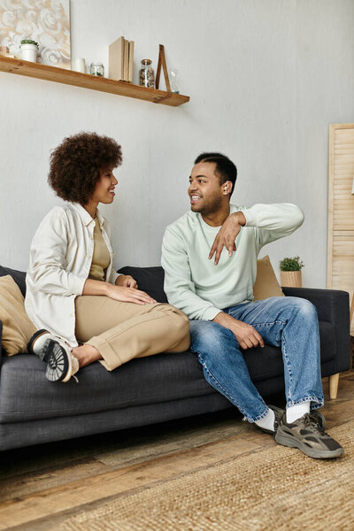 Афроамериканская пара сидит дома на диване, общаясь на языке жестов.