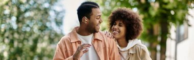 Afro-Amerikalı bir çift parkta gülümsüyor ve birbirlerine işaret veriyorlar..