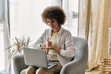 An African American woman signs with her hands while sitting in a chair and using a laptop. clipart