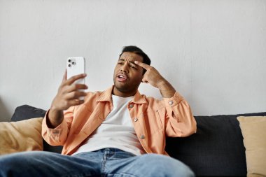Kanepede oturan bir adam, telefonuyla video sohbeti yaparken işaret dili kullanıyor..