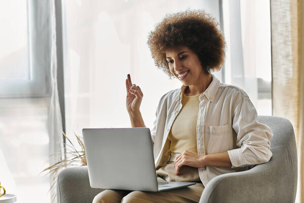 An attractive woman uses sign language while sitting in her living room, next to laptop.
