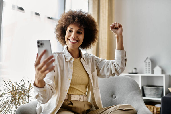 Женщина сидит дома на диване, улыбается и подписывается телефоном..