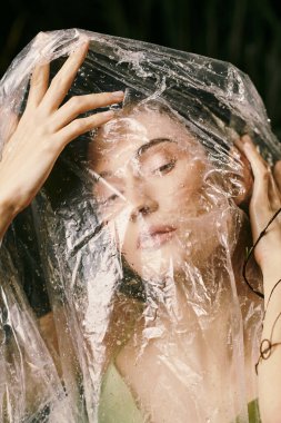 Çekici bir kadın bataklığın yanında estetik bir kıyafet içinde poz veriyor. Yüzü plastik ambalajla kaplanmış..