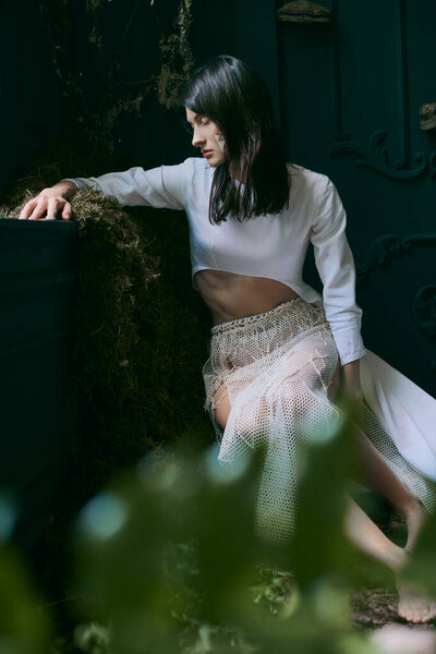 A woman in a white dress poses near a swamp.