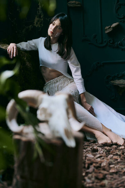 Woman in white clothing poses against dark background.
