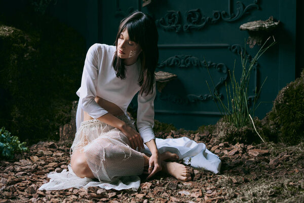 A woman sits, looking sad, dressed beautifully.