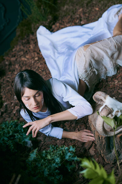 A woman in flowing white garments reaches out towards a swamp.
