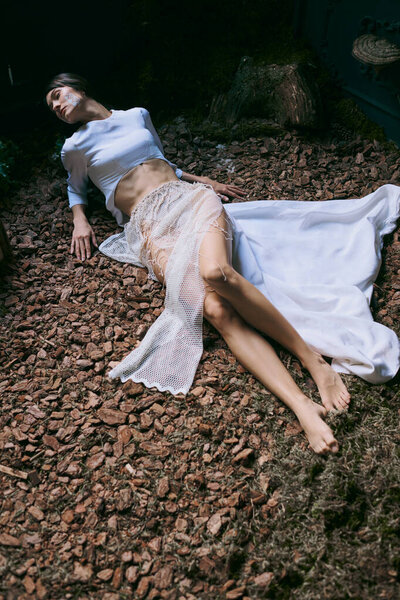 Женщина в эфирной одежде позирует на кровати из древесной щепы.