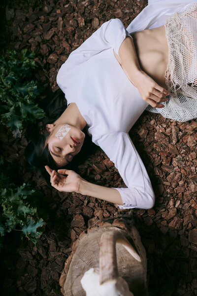A woman lies on ground, her white clothes contrasting the landscape.