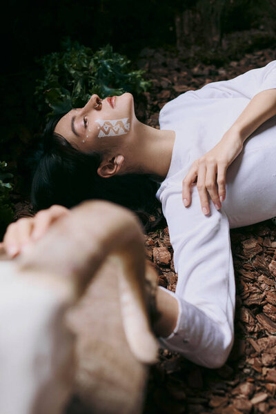 Woman lies near swamp with painted face.