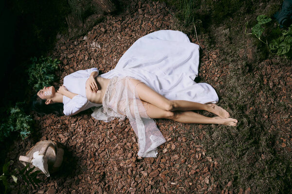 A woman lies in a forest clearing, her white dress flowing around her.
