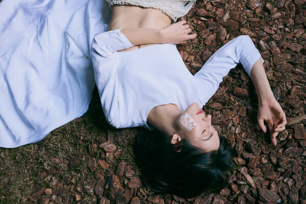 Woman in white clothes lies in forest.
