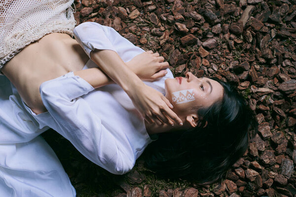 A woman in white clothing lies on the ground near a swamp.