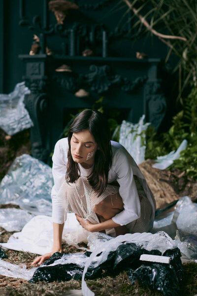 A woman in white clothing poses amidst a swamp of plastic garbage.