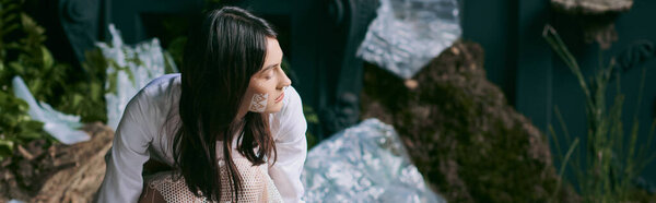 Woman in white lace dress in swamp, staring at plastic garbage.