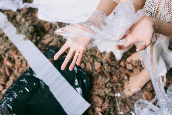 Женская рука появляется из кучи пластиковых отходов, видна только ее рука..