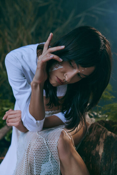 Женщина в белой одежде сидит в болоте, ее лицо мрачно.