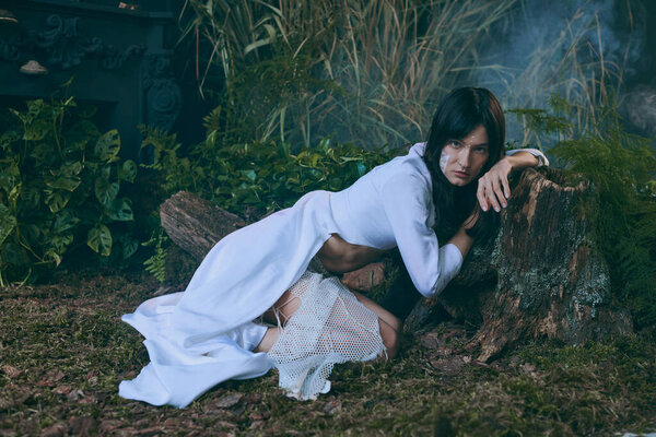 A woman in a flowing white dress poses near a swamp.