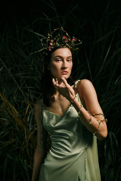 Woman in green dress gracefully poses in forest with floral crown.