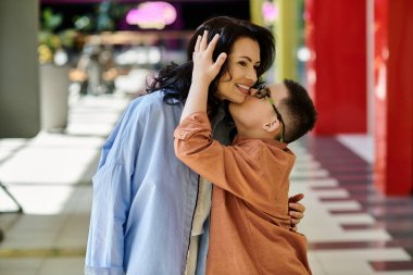 A mother and her son with Down syndrome kissing in a shopping mall and share a loving embrace. clipart