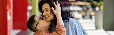 A mother and her son with Down syndrome share a loving moment while walking through a shopping mall. clipart