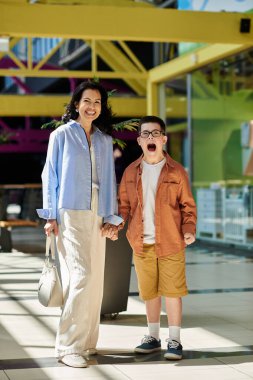 Down sendromlu bir anne ve oğlu alışveriş merkezinde el ele yürüyorlar, gülümsüyorlar ve birlikte vakit geçiriyorlar..