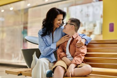 A mother and her son with Down syndrome share a tender moment while sitting on a bench in a shopping mall. clipart