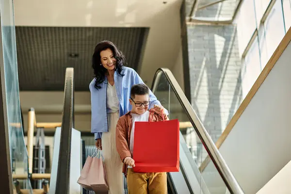 stock image A mother and her son with Down syndrome enjoy a day of shopping at the mall, riding the escalator and carrying shopping bags.