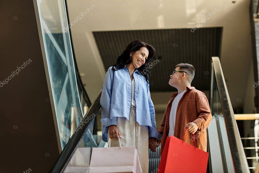 A mother and her son with Down syndrome smile and hold hands while walking up an escalator in a shopping mall.