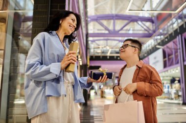 A mother and her son with Down syndrome smile and exchange gifts while walking through a shopping mall. clipart