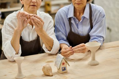 Two mature women work on pottery projects in a cozy art studio. clipart