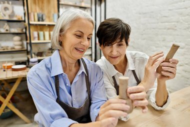 Two mature lesbian women working on pottery in a cozy art studio. clipart