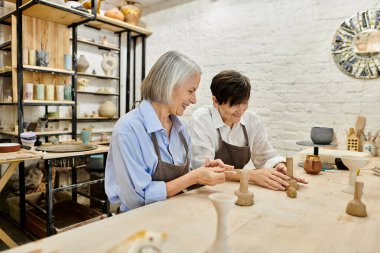 A senior lesbian couple works together on pottery in a light-filled studio. clipart