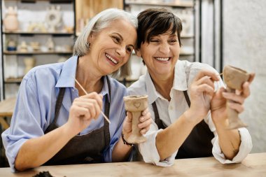 Çömlek atölyesindeki iki kadın kil eserlerini boyuyor..